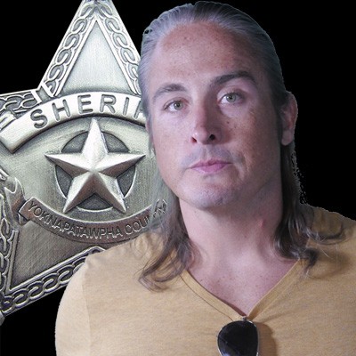 Man with shoulder-length graying hair pulled back, with a sheriff's star in the background